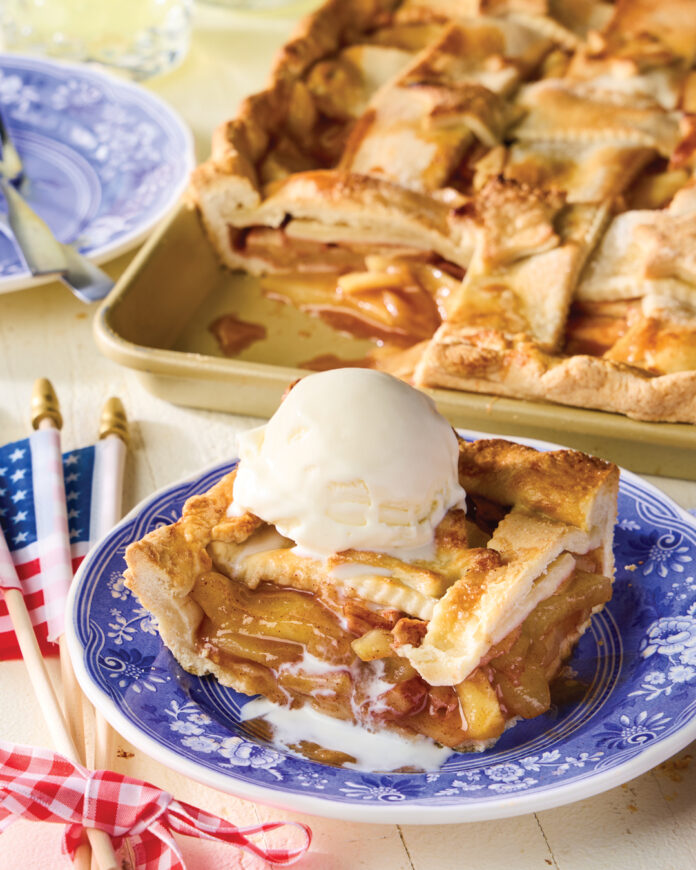 Sheet pan apple pie with a lattice crust topped with a scoop of vanilla ice cream.